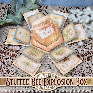 May include: A handmade explosion box with a honey jar illustration at the center. The box features floral illustrations on each panel, with a light blue border. The box is labeled "Honey" and "Stuffed Bee Explosion Box Printables".