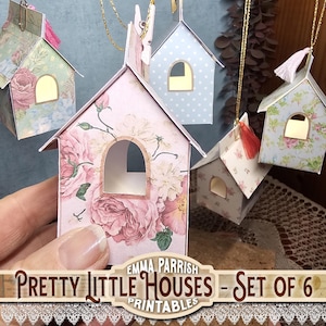 May include: A set of six miniature paper houses, each with an arched window, suspended by gold cords. The houses are decorated with floral patterns in pink, blue, and white. The text "Pretty Little Houses - Set of 6 Printables" is displayed.
