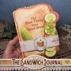 May include: A die-cut journal shaped like a sandwich with toasted bread slices, a pickle, cucumber slices, and tomato. The cover features the text The Best Thing Since Sliced Bread and a circular label with a club sandwich illustration and text.
