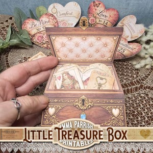 May include: A decorative wooden treasure box with a tufted interior, filled with cards and tags. The box is adorned with gold accents and heart-shaped details. Heart-shaped tags with phrases like "Be Mine" and "Love" are arranged behind the box. The text "Little Treasure Box Printables" is at the bottom.