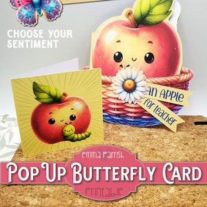 May include: Printable pop-up card featuring a red apple with a green leaf and a smiling face. The apple is in a basket with a white daisy and a banner that says "An Apple for Teacher". The card also includes a butterfly with blue and pink wings.