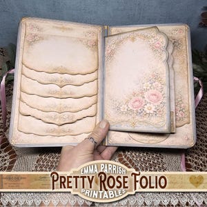 Puede incluir: Diario abierto con páginas decorativas. Las páginas tienen una estética vintage con diseños florales y ornamentales. La paleta de colores del diario incluye rosas suaves, cremas y toques dorados. El texto "Pretty Rose Folio Printables" es visible.