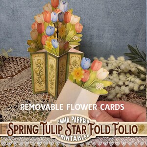 Może przedstawiać: Karta pop-up w kształcie gwiazdy z bukietem tulipan&oacute;w w kolorach r&oacute;żowym, pomarańczowym i niebieskim. Karta zawiera tekst "Spring Tulip Star Fold Folio" i "Removable Flower Cards". Unikalny wz&oacute;r kwiatowy.
