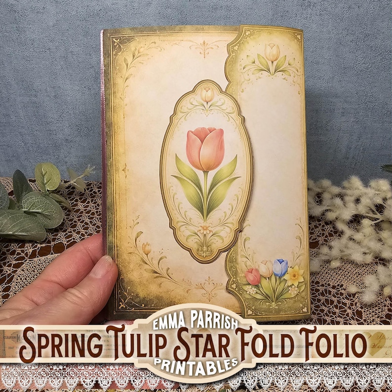 Może przedstawiać: Folio w stylu vintage z ilustracją r&oacute;żowego tulipana w owalnej ramie. Okładka ma kremowe tło z kwiatowymi akcentami i tekstem "Spring Tulip Star Fold Folio". Folio jest trzymane przez rękę.