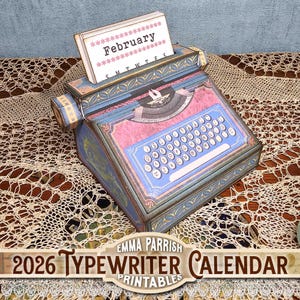 May include: A decorative typewriter calendar for 2026, featuring a blue and pink design with gold accents. The calendar displays the month of February. The product is labeled "Emma Parrish Printables".