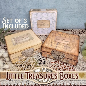 May include: Three decorative wooden boxes with metal detailing. Each box features a label that reads "TINY TREASURES". The boxes are in shades of brown and beige, with a floral patterned box at the back. The text "SET OF 3 INCLUDED" is visible.