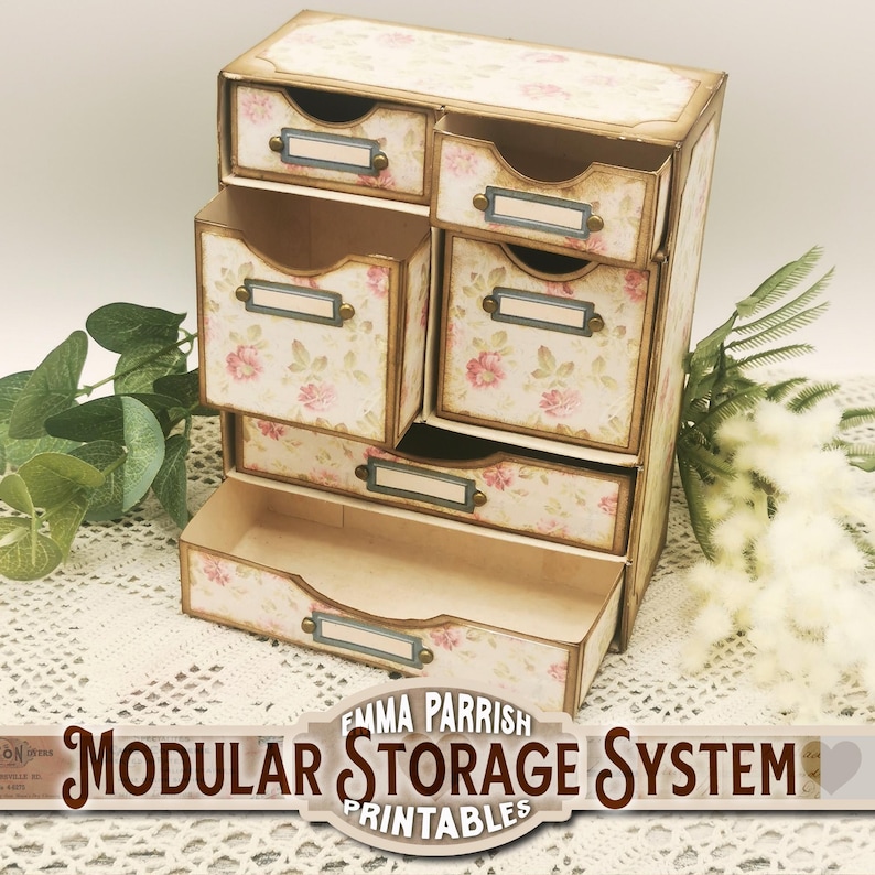 May include: A vintage-style modular storage system with drawers featuring a floral pattern. The drawers have labels and brass-colored hardware. The system is made of cardboard and is labeled "Emma Parrish Modular Storage System Printables".