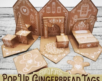 May include: A set of brown paper pop-up gingerbread house tags featuring white line art of windows, hearts, stockings, and furniture. The set includes a flat gingerbread person cutout and a folded house structure with interior details.