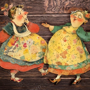 May include: Two vintage paper cutouts of women in colorful dresses. The figures have rosy cheeks and are set against a dark wood background. The dresses feature floral patterns and are trimmed with red and blue accents. The women appear to be dancing.