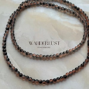 Può includere: Una collana di perle di pietre preziose nere e marroni. Le perle sono piccole e rotonde e sono infilate su un filo trasparente. Le perle sono disposte in un design semplice ed elegante.