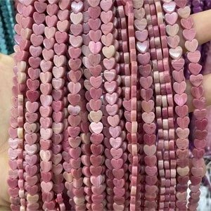 May include: A strand of pink heart-shaped beads made from natural stone. The beads are strung on a clear thread and are ready to be used for jewelry making.