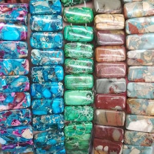 May include: A collection of rectangular gemstone beads arranged in four vertical strands. The beads feature varied marbled patterns in shades of bright blue, deep turquoise, vibrant green, and earthy tones of brown, tan, and muted red with veining.