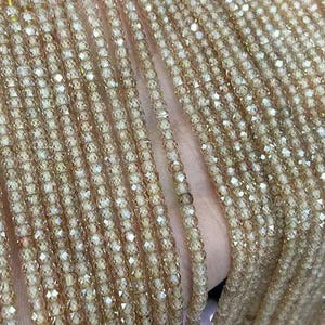 May include: A strand of iridescent gold glass beads. The beads are small and round, with a faceted finish. The strand is long and thin, and the beads are strung closely together.