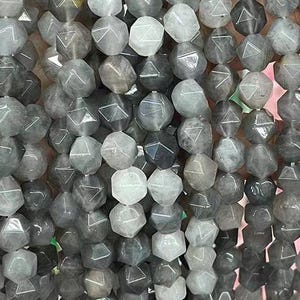 May include: A strand of grey faceted gemstone beads. The beads are shaped like a six-sided die with a triangle etched on each side.