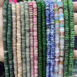 May include: A collection of colorful gemstone beads in various shades of green, pink, blue, and white. The beads are strung together, showcasing their round, flat shape. The image displays a variety of natural stone beads, perfect for jewelry making.