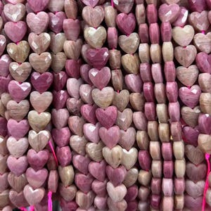 May include: Strands of heart-shaped beads in varying shades of pink and tan. The beads are strung together, creating a textured surface. The heart beads have a faceted appearance, catching the light. The beads are likely for jewelry making.