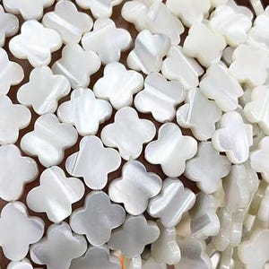 Può includere: Perle bianche di madreperla a forma di trifoglio. Le perle sono infilate e hanno una finitura liscia e lucida.