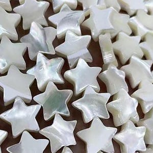 Peut inclure: Gros plan sur une collection de carreaux en forme d'étoile blancs irisés. Les carreaux sont en nacre et ont un aspect naturel et organique.