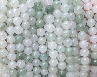 Puede incluir: Primer plano de una hebra de cuentas de jade blanco y verde. Las cuentas son redondas y lisas, y tienen un brillo sutil.