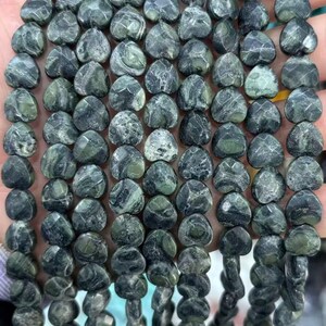 May include: Strands of heart-shaped beads in shades of green and gray. The beads have a marbled appearance, with variations in color and texture. The beads are strung together, creating a necklace or bracelet.