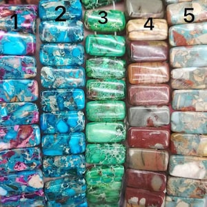 May include: Close-up of a collection of rectangular gemstone beads in various colors. The beads are arranged in vertical columns, showcasing a range of hues including turquoise, green, brown, and pink. Each bead has a polished, smooth surface.