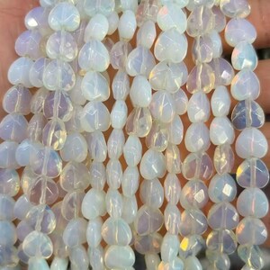 May include: Strands of opalescent heart-shaped beads. The beads have a soft, pearly white color with subtle iridescent flashes. The beads are strung together, creating a flowing, textured appearance. Ideal for jewelry making.