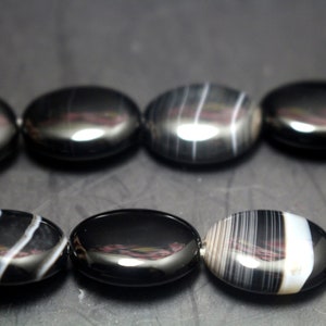 May include: A strand of black and white agate beads. The beads are oval shaped and have a high polish.