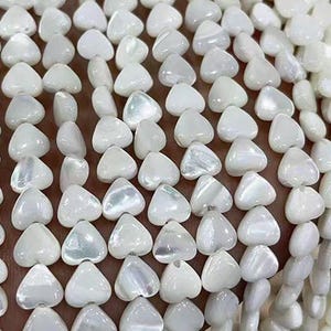 Peut inclure: Un brin de perles en forme de cœur en coquillage blanc. Les perles ont une finition nacrée et sont enfilées sur un fil transparent.