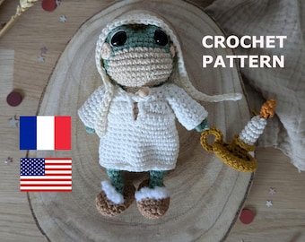 May include: A crocheted doll with a green head, large black eyes, and a beige face covering. It wears a white robe and brown shoes with white trim. The doll holds a yellow candle. The text "CROCHET PATTERN" is visible.