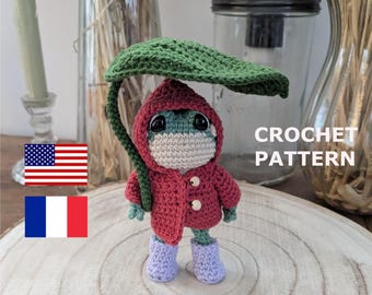 May include: Crochet pattern for a green frog wearing a red hooded jacket and a green leaf umbrella. The frog is wearing purple boots and has a white face mask.
