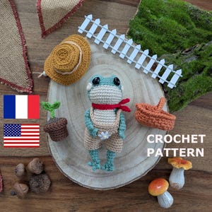 Peut inclure: Une poupée grenouille au crochet portant une salopette et une écharpe rouge, avec un petit chapeau, un panier et une plante. La grenouille est bleu clair et beige. L'image comprend également une clôture blanche et les mots "CROCHET PATTERN".