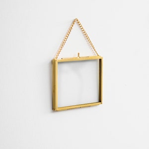 Pode incluir: Um quadro de fotos de metal dourado com frente de vidro e uma corrente de suspensão. O quadro está vazio.