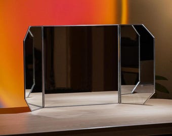 May include: A three-sided, octagonal-shaped mirror with a silver frame. The mirror is sitting on a wooden table.
