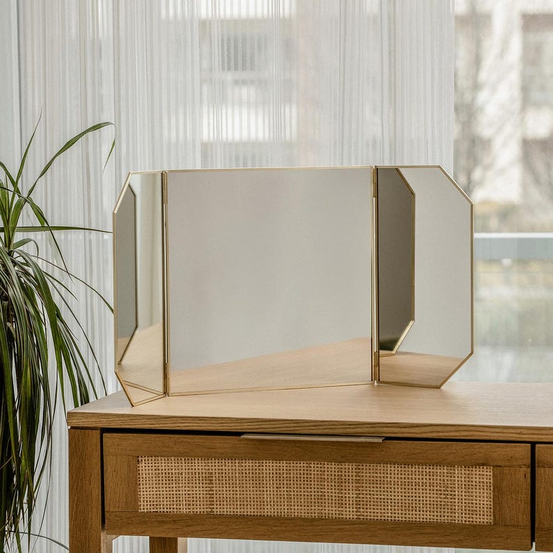 May include: A gold-framed, three-panel vanity mirror with a wooden vanity table with a woven wicker drawer.