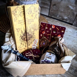 Op de afbeelding: Een thematisch cadeaupakket met een boek, notitieboek, ketting, klein zakje, pot en flesstopper. De items zijn gerangschikt in een bruine kartonnen doos, met perkamentpapier. Het boek heeft een kaartontwerp.