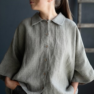 Può includere: Una camicia di lino a righe grigie e bianche con colletto e chiusura con bottoni. La camicia ha una vestibilità rilassata e maniche a tre quarti.