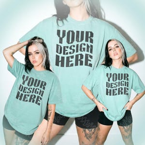 May include: A light teal t-shirt with the text "YOUR DESIGN HERE" in black block letters. The t-shirt is worn by a person. The person is wearing black shorts. The background is white.