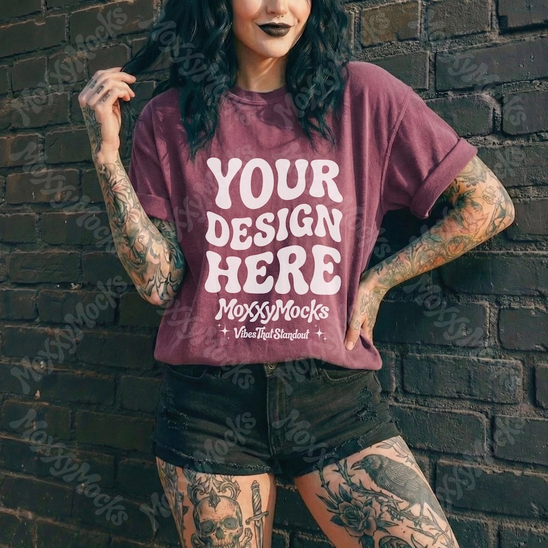 May include: A maroon t-shirt with the text "YOUR DESIGN HERE" in a white, retro font. The shirt has rolled-up sleeves and is part of a mock-up, with the brand name "MoxxyMocks" and tagline "Vibes That Standout" at the bottom.