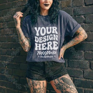 May include: A dark gray t-shirt with the text "YOUR DESIGN HERE" in white, along with the brand name "MoxxyMocks" and the tagline "Vibes That Standout". The shirt is paired with black shorts.