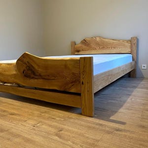 Puede incluir: Una estructura de cama de madera con un aspecto natural sin terminar. El cabecero y el piecero presentan la forma orgánica de la madera, con un colchón azul claro. La cama está sobre un suelo de madera.