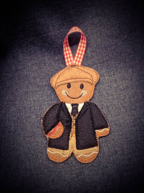 A handmade felt gingerbread man dressed as a dapper 1920s gentleman with a flat cap — charmingly specific and clearly stitched by human hands.