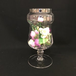 Peut inclure: Un vase en verre transparent avec une base large et un col étroit, rempli de fleurs violettes et blanches.