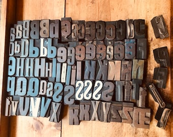 Op de afbeelding: Een verzameling vintage houten letterpersdrukblokken in verschillende maten en stijlen. De blokken zijn alfabetisch gerangschikt en bevatten zowel hoofdletters als kleine letters, evenals cijfers.