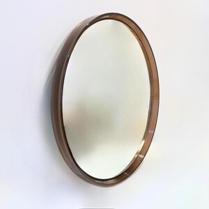 May include: A circular wall mirror featuring a reflective glass surface encased in a deep, translucent brown tinted frame. The frame has a smooth, rounded edge and a glossy finish, creating a distinct border around the central circular mirror.