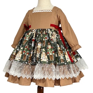 May include: A brown and green dress with a square neckline and long sleeves. The bodice is brown, and the skirt features a print of nutcrackers on a green background. Red ribbons accent the waist, and white lace trim the hem.
