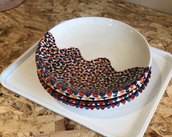 May include: A set of four white ceramic bowls with a colorful, speckled design. The bowls are stacked on top of each other and have a wavy, uneven edge.