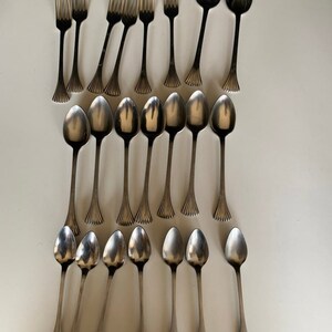 May include: A set of silver-toned teaspoons with decorative handles. The spoons are arranged in rows, with the handles pointing upwards.