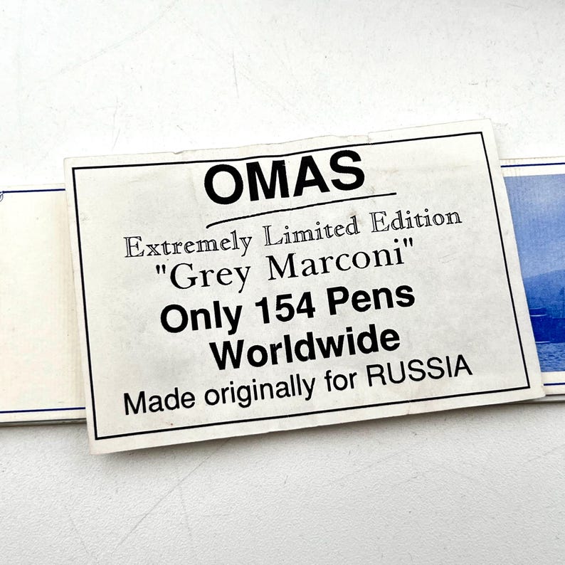Puede incluir: Primer plano de una tarjeta rectangular blanca con la palabra "OMAS" en la parte superior. La tarjeta dice "Edici&oacute;n Extremadamente Limitada 'Grey Marconi' Solo 154 Plumas en Todo el Mundo Hecho originalmente para RUSIA."