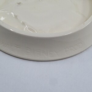 May include: White ceramic dish with a raised rim and the text "Walt Disney Prod" on the bottom.