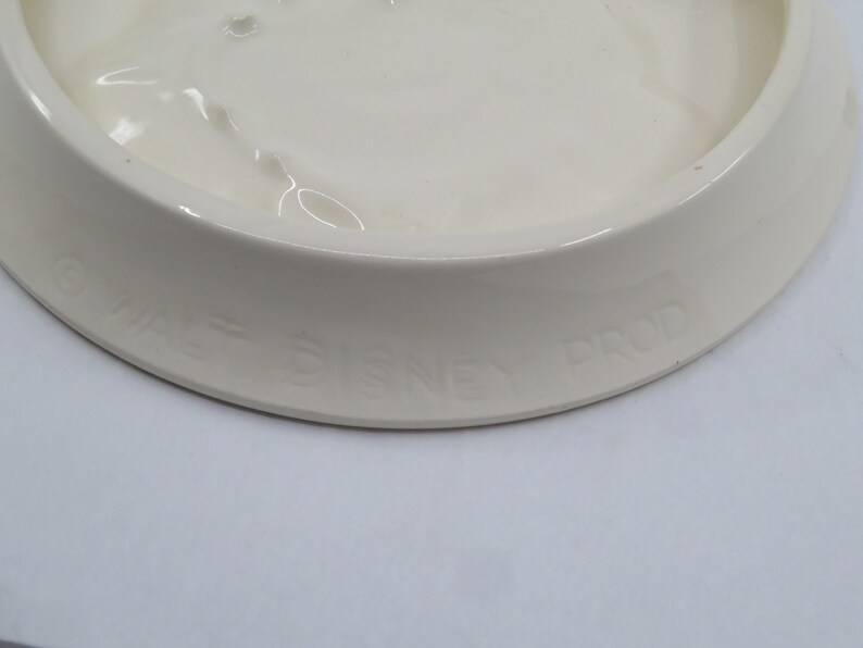 May include: White ceramic dish with a raised rim and the text "Walt Disney Prod" on the bottom.